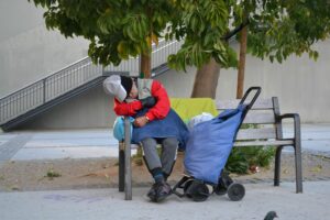 Un sense sotre dorm en un banc al costat de l'Avinguda Maria Cristina