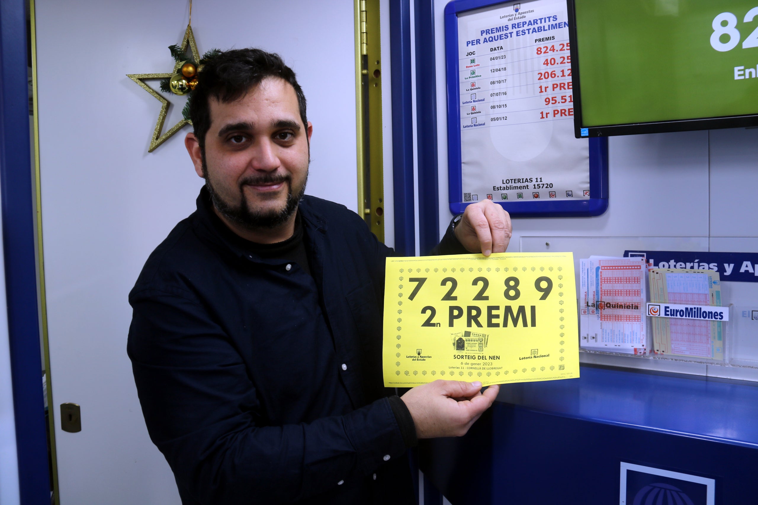 l'Albert, propietari de l'administració de loteria número 11 de Cornellà de Llobregat, amb el cartell del segon premi de la rifa de Reis   Data de publicació: divendres 06 de gener del 2023, 14:13  Localització: Cornellà de Llobregat  Autor: Àlex Recolons