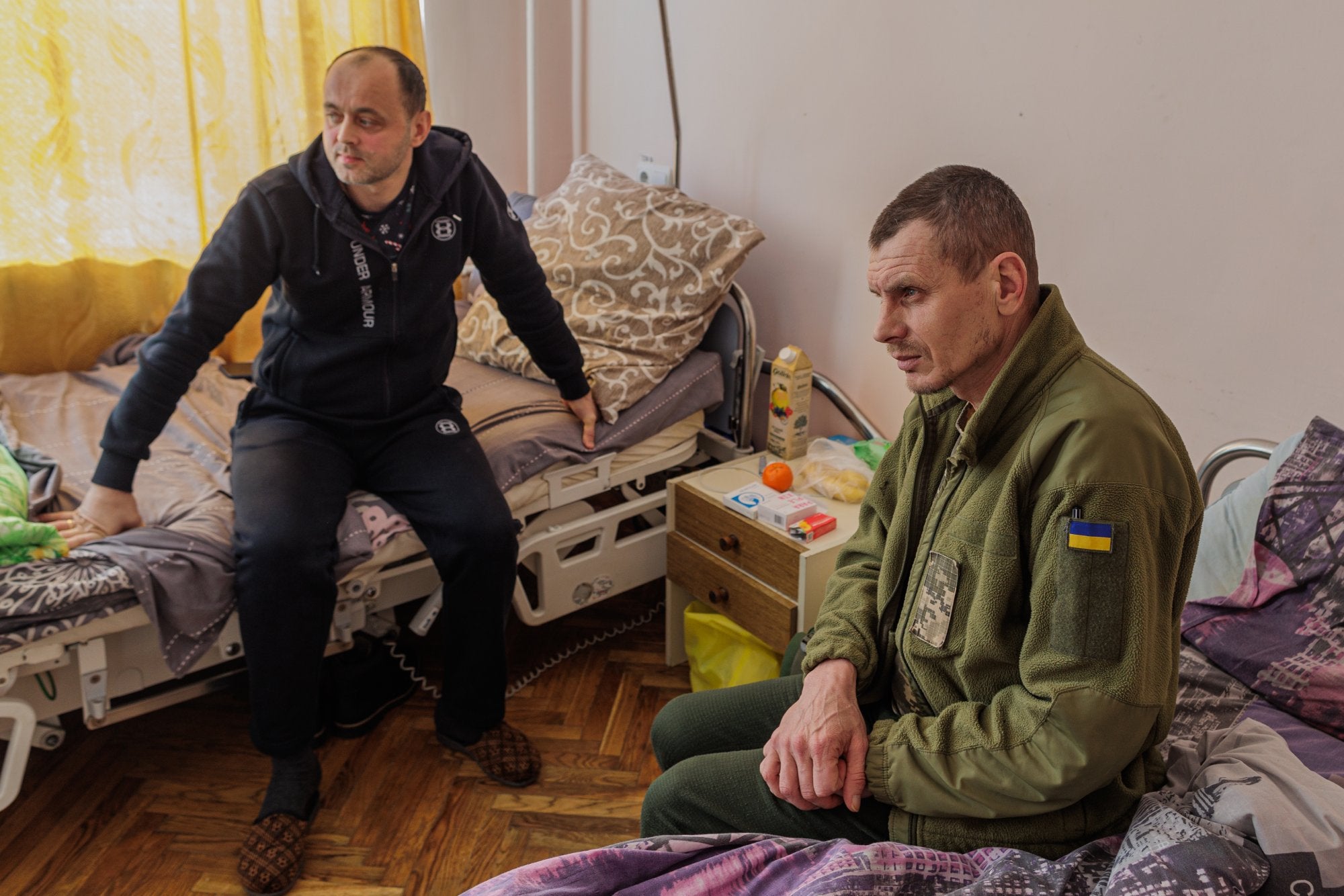 A l'esquerra Stephan, soldat de la 8a i 10a brigada d'assalt de Lviv a qui van mobilitzar dos dies després de l'inici de la guerra, el 26 de febrer. Juntament amb la brigada va dur a terme diverses tasques de combat fins que, el 3 de desembre, va ser ferit al cap durant una batalla a la regió de Luhansk. Sergei, a la dreta, vestit amb un xandall color verd militar, va resultar ferit després de l'1 d'agost del 2014. Des d'aleshores, la seva salut ha empitjorat. Declara que, des de llavors, la seva salut física i mental ha anat empitjorant progressivament.