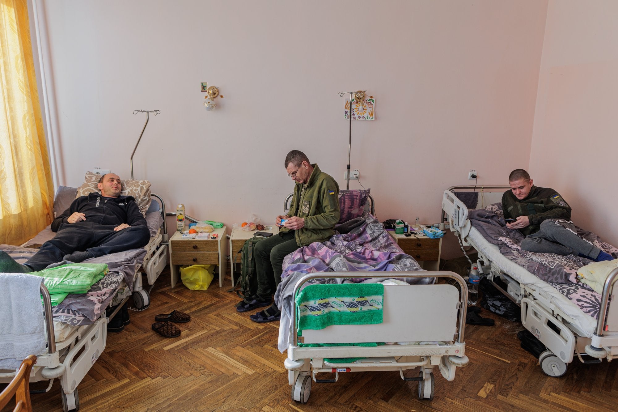 Tot i que aquest és un hospital públic, la guerra ha canviat la prioritat d'atenció als pacients. Segons Iryna, doctora a l'hospital de Truskavets, atenen tots els pacients que arriben, siguin aquests civils o militars. Tot i això, es prima oferir serveis de rehabilitació a militars i, segons la doctora, els civils ho entenen i comparteixen. En aquesta habitació s'allotgen (d'esquerra a dreta): Stephan, Sergei i Yuri, combatents ferits al front que actualment es troben en rehabilitació.