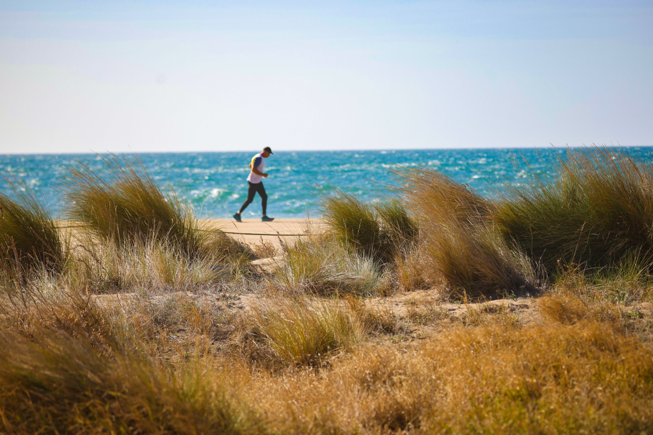Un home vestit amb roba esportiva caminant per la platja de Castelldefels / AMB