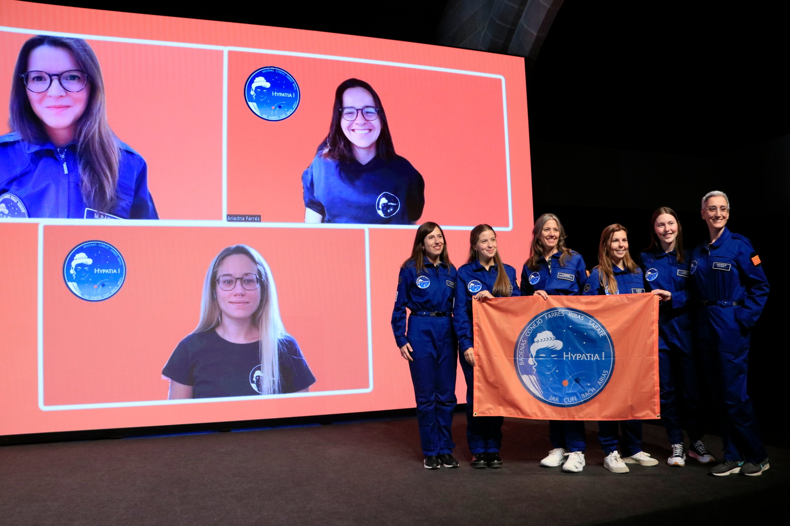 Les nou integrants d'Hypatia I en la presentació a Barcelona de la missió de científiques catalanes a l'estació anàloga de Mart al desert de Utah, als Estats Units, amb la vestimenta i la bandera oficial.   Data de publicació: dimecres 12 d’abril del 2023, 13:58  Localització: Barcelona  Autor: Laura Fíguls Barnaus
