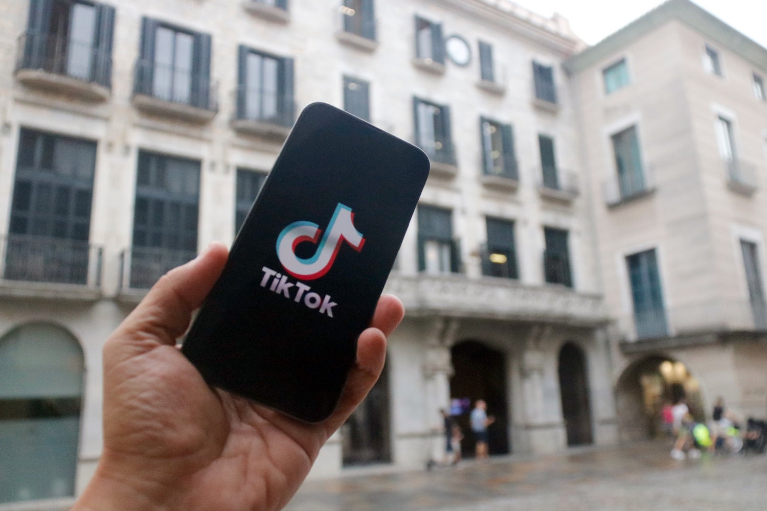 En primer terme, un mòbil amb el logotip d'una xarxa social; al fons, la façana de l'Ajuntament de Girona /  Xavier Pi - ACN
