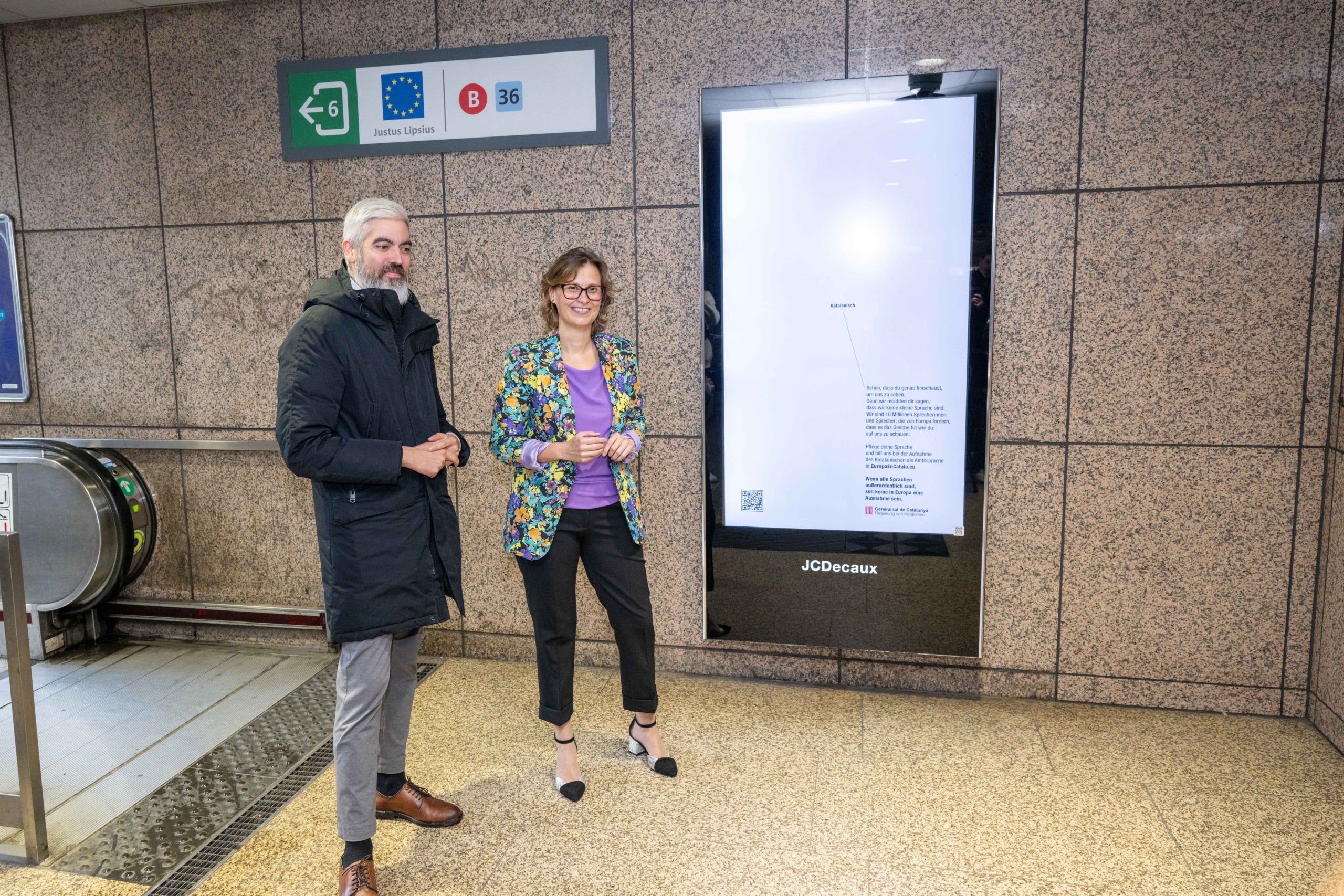 La consellera Meritxell Serret i el delegat davant la UE, Ignasi Centelles, a la parada de metro Schuman a Brussel·les, on hi ha instal·lat un anunci