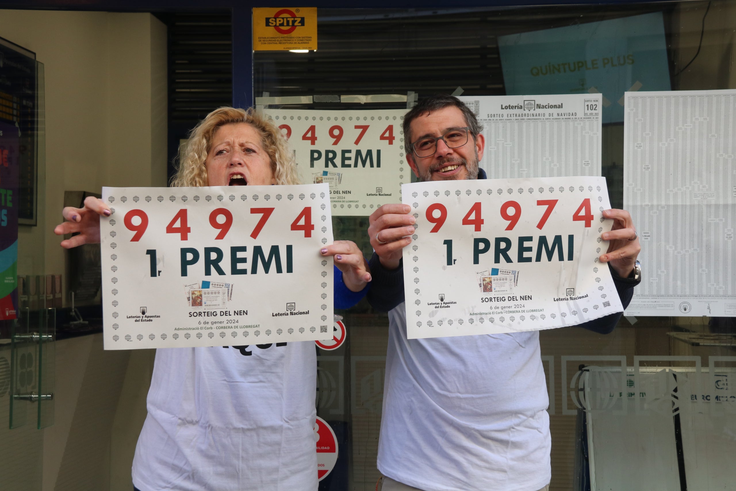 El propietari i una treballadora de l'administració de loteria de Cornellà amb cartells del primer premi del sorteig de Reis / ACN