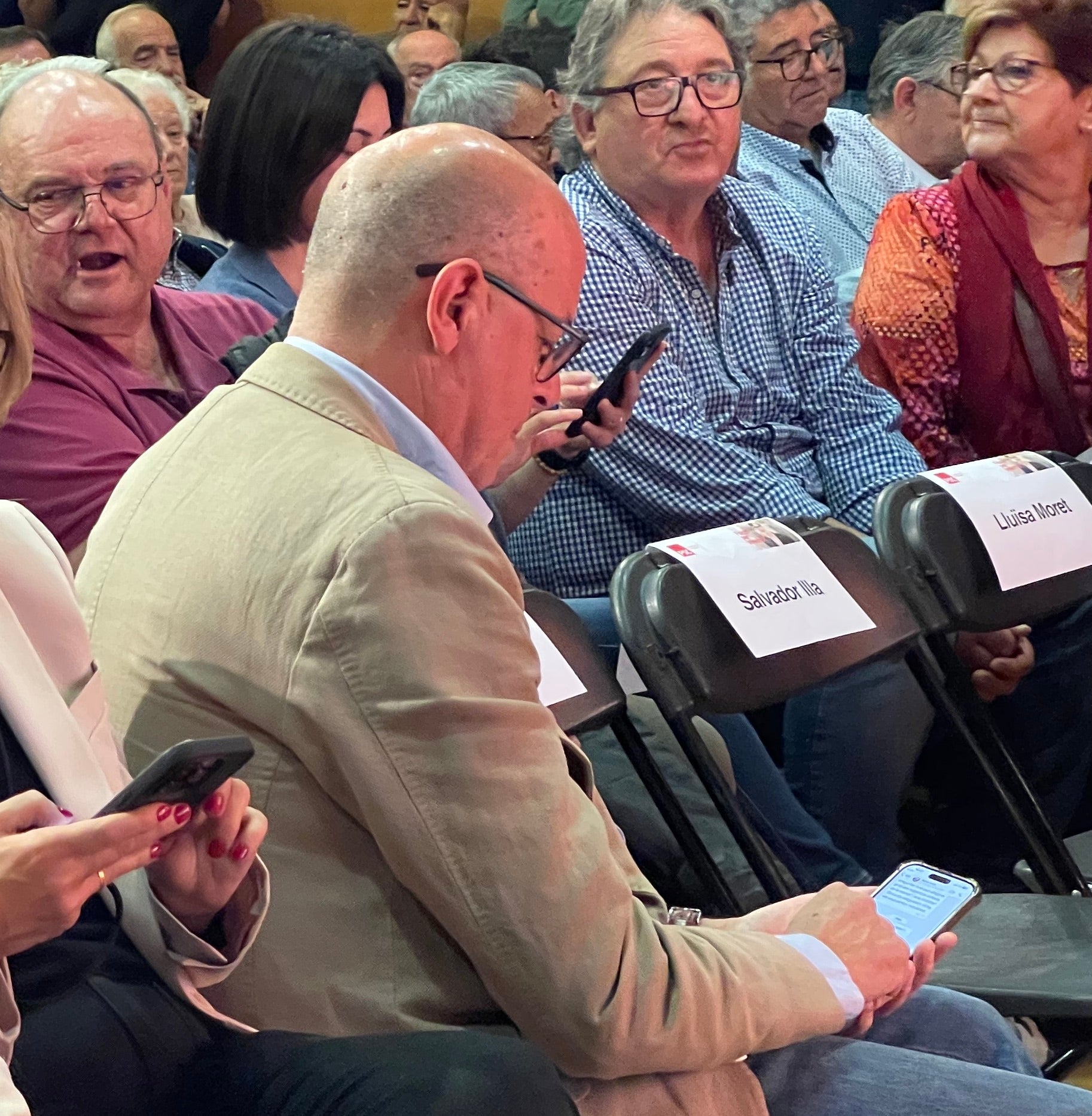 José Zaragoza mira el seu mòbil, mentre seu a primera fila en el míting del PSC a l'Hospitalet/Quico Sallés