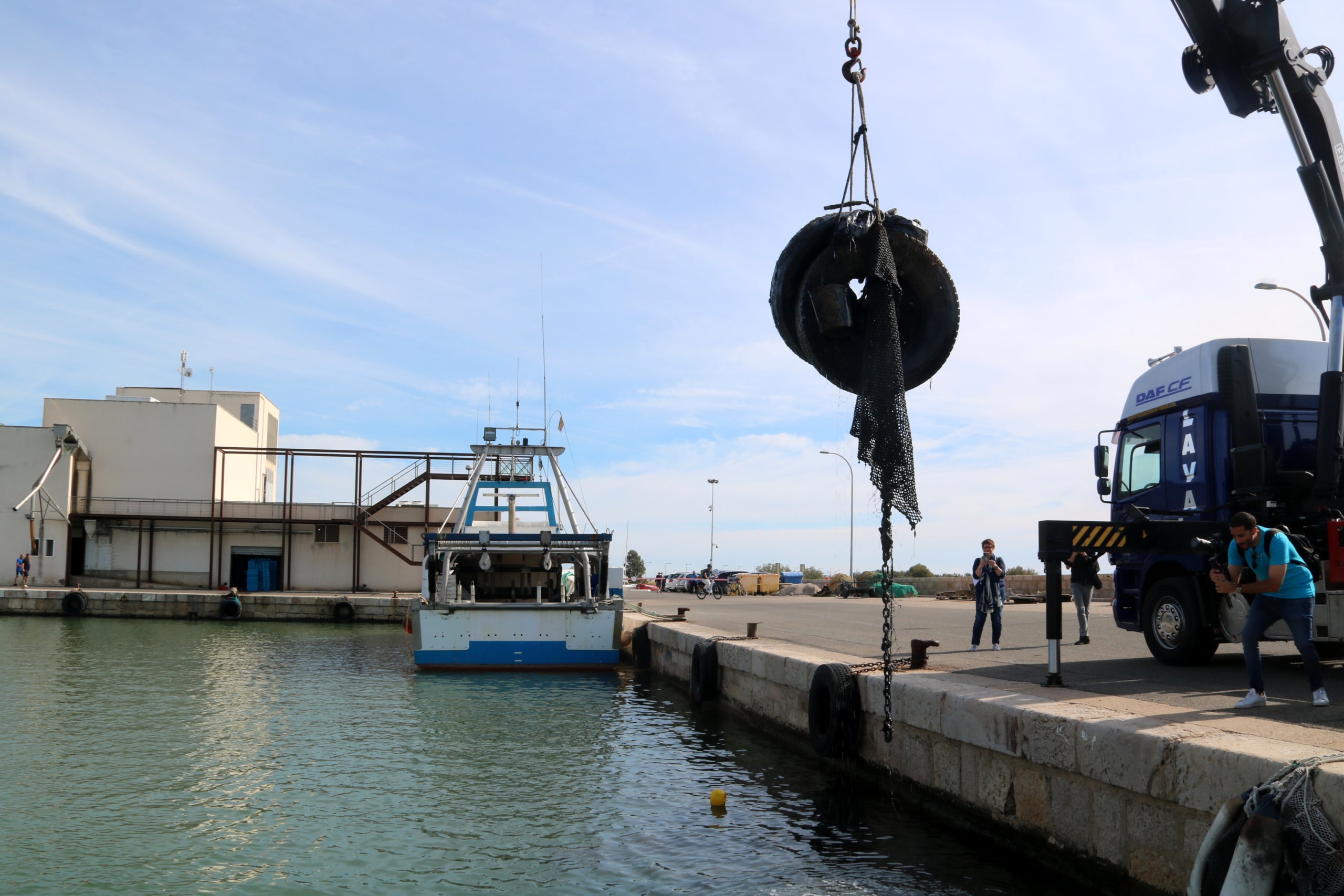 Una grua retira rodes i malles que un bussejador ha ajudat a agafar del fons marí del port de la Ràpita | Anna Ferràs (ACN)