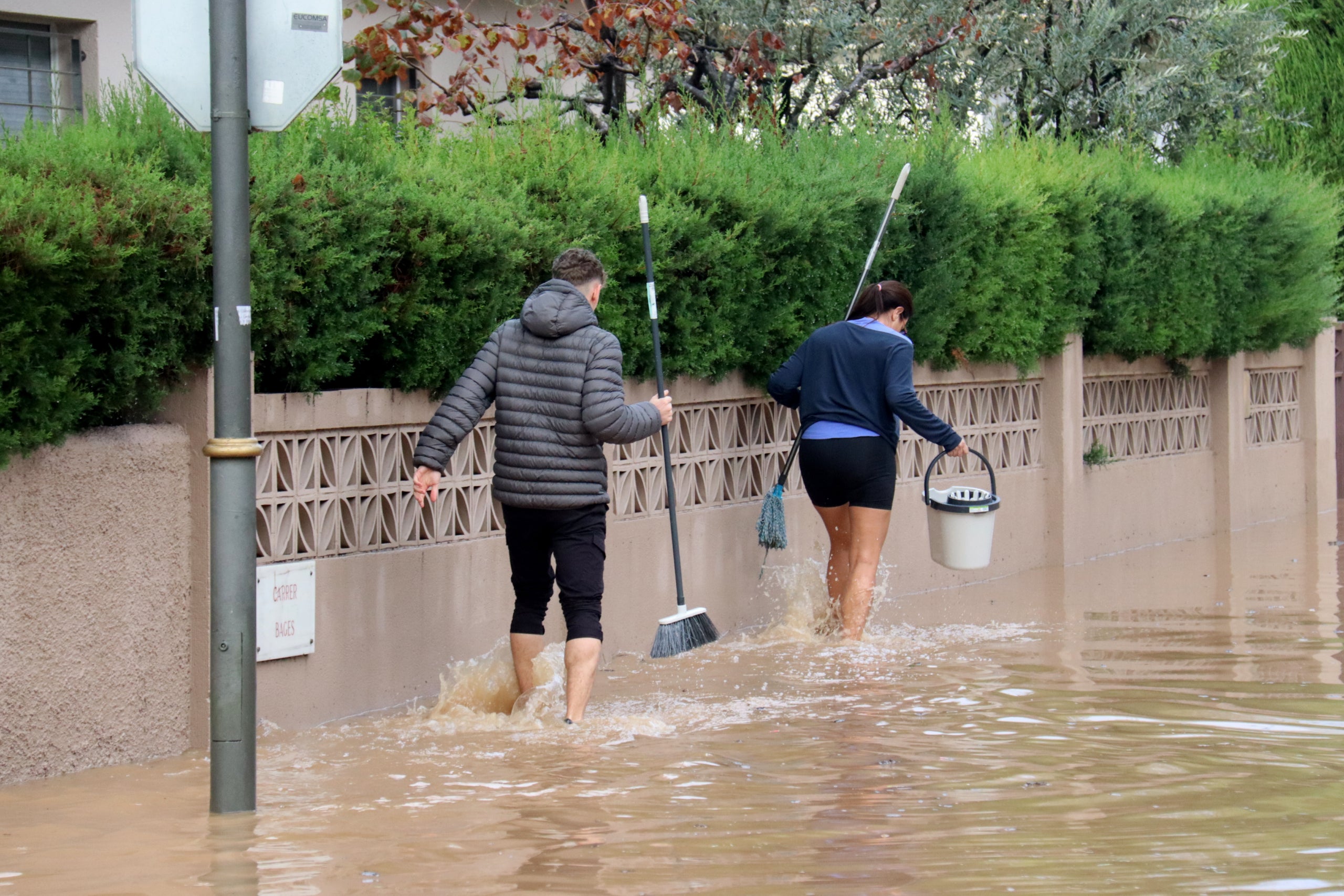 Un home i una dona caminant amb cubells per un dels carrers inundats de la urbanització La Móra de Tarragona | Neus Bertola (ACN)