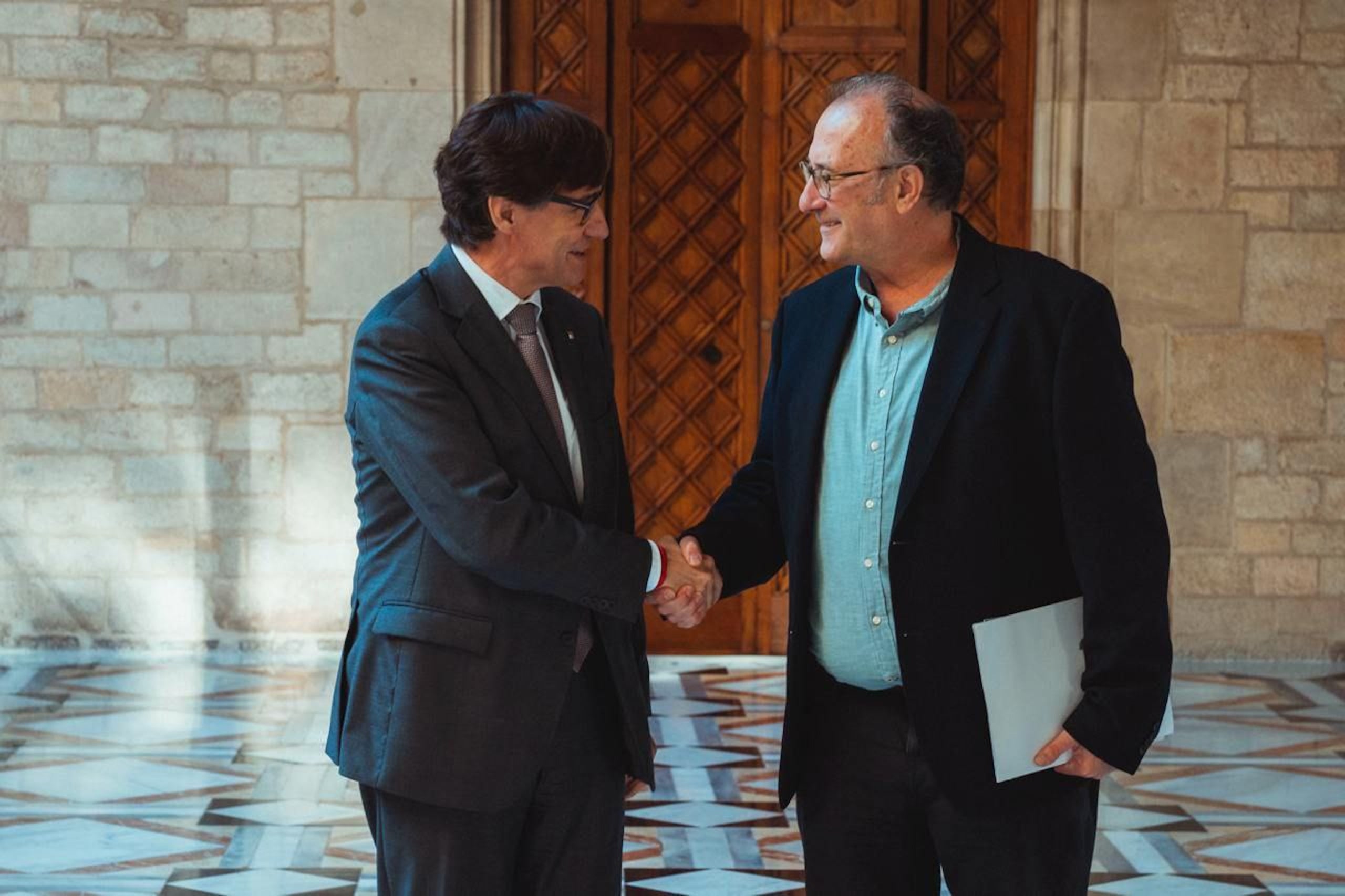 El president de la Generalitat, Salvador Illa, encaixant mans amb el president d'Òmnium Cultural, Xavier Antich, abans de reunir-se / Arnau Carbonell / Govern