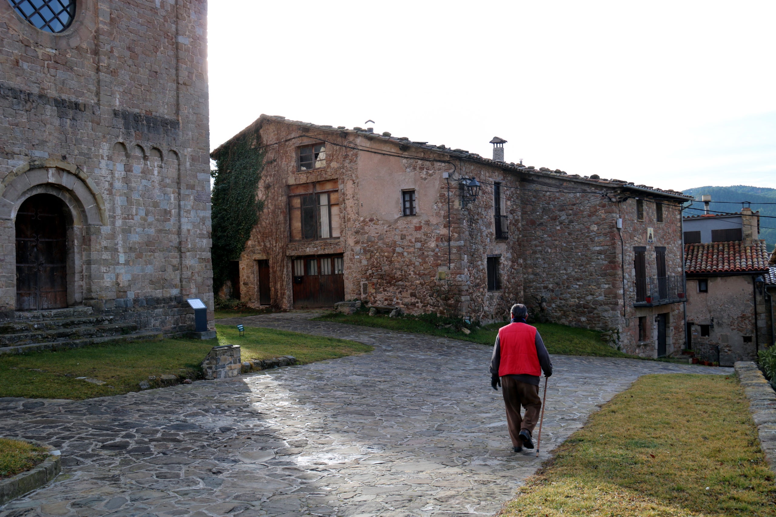 Un dels pocs veïns de Sant Jaume de Frontanyà passeja davant la rectoria, on ara l'Ajuntament vol impulsar el restaurant | Nia Escolà (ACN)