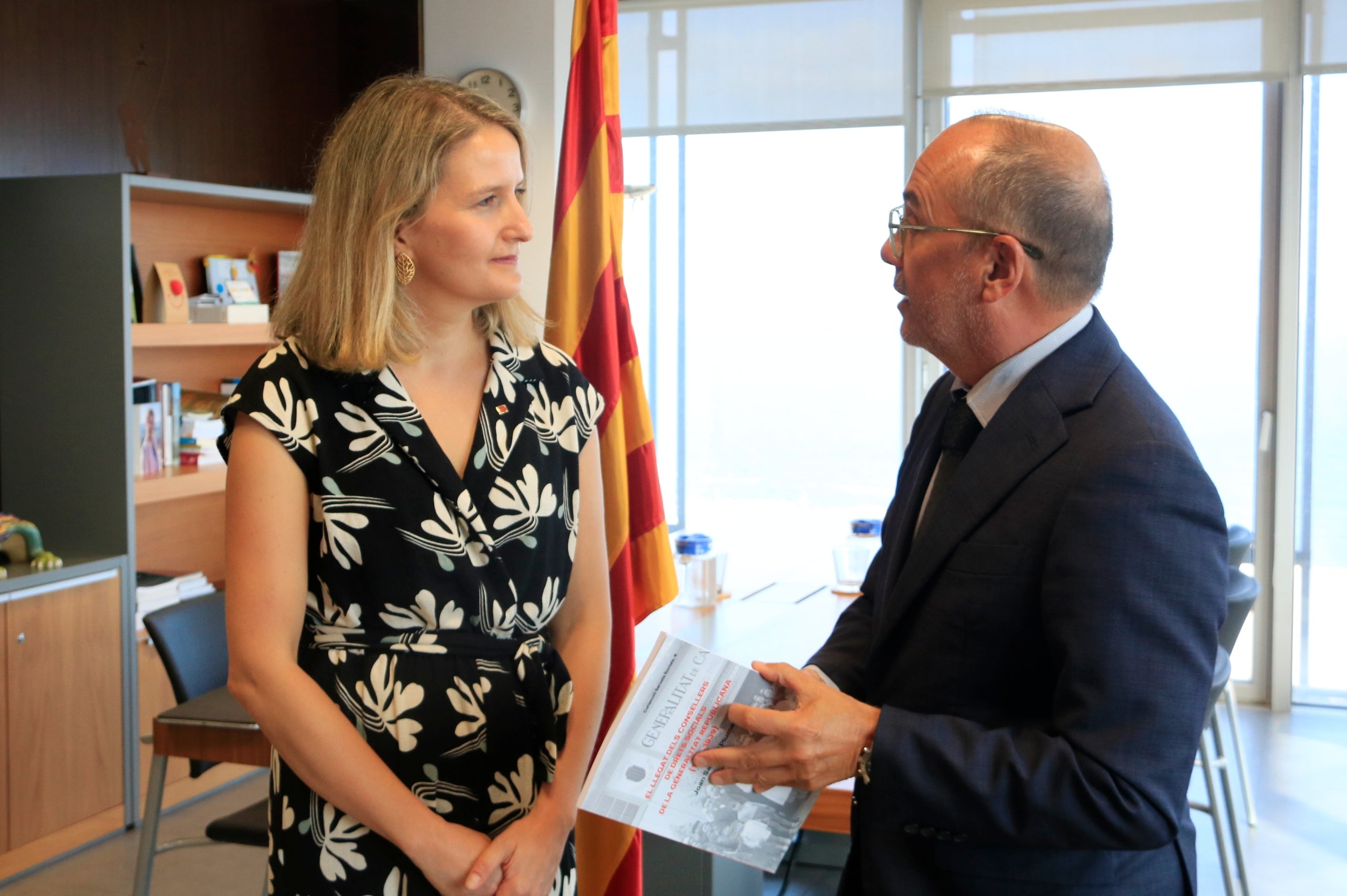 La consellera de Drets Socials i Inclusió, Mónica Martínez Bravo, amb el seu antecessor, Carles Campuzano, que li regala un llibre sobre el llegat dels consellers de Drets Socials de la Generalitat republicana, en el traspàs de cartera / ACN