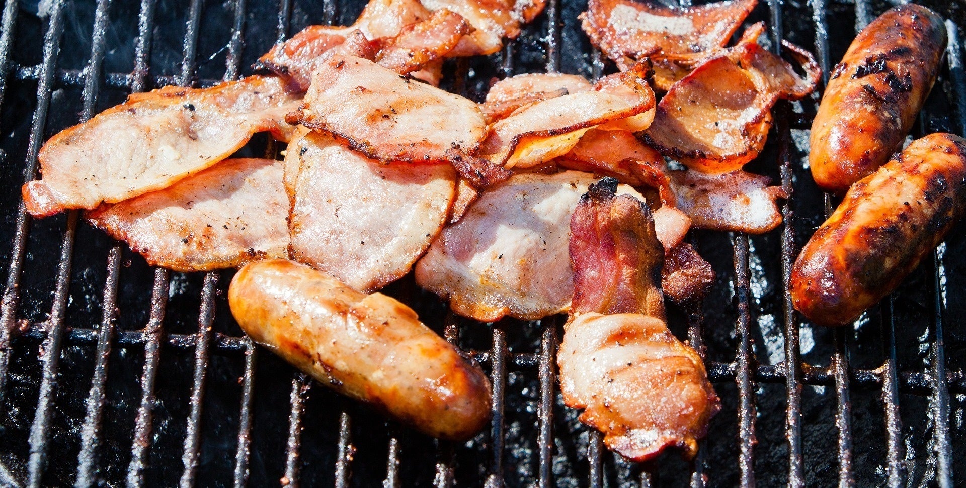 Imatge d'arxiu de salsitxes i bacó sobre una graella de barbacoa / Europa Press