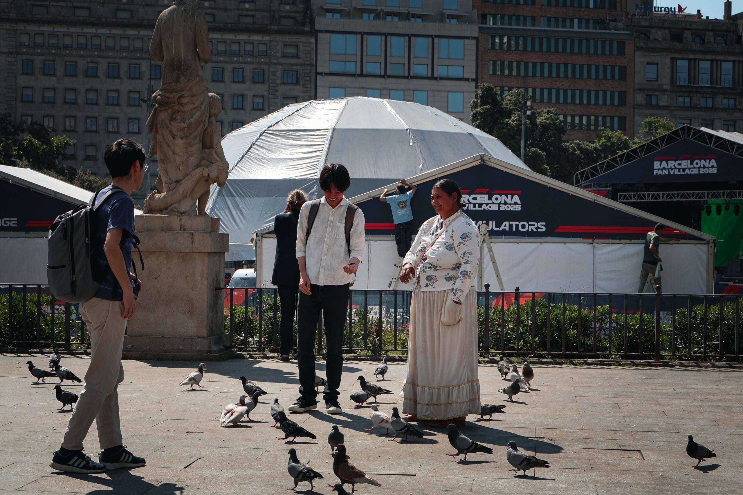 Turisme i calor. Turistes interactuen amb els coloms a la Plaça de Catalunya a Barcelona. / Marta Cardenal