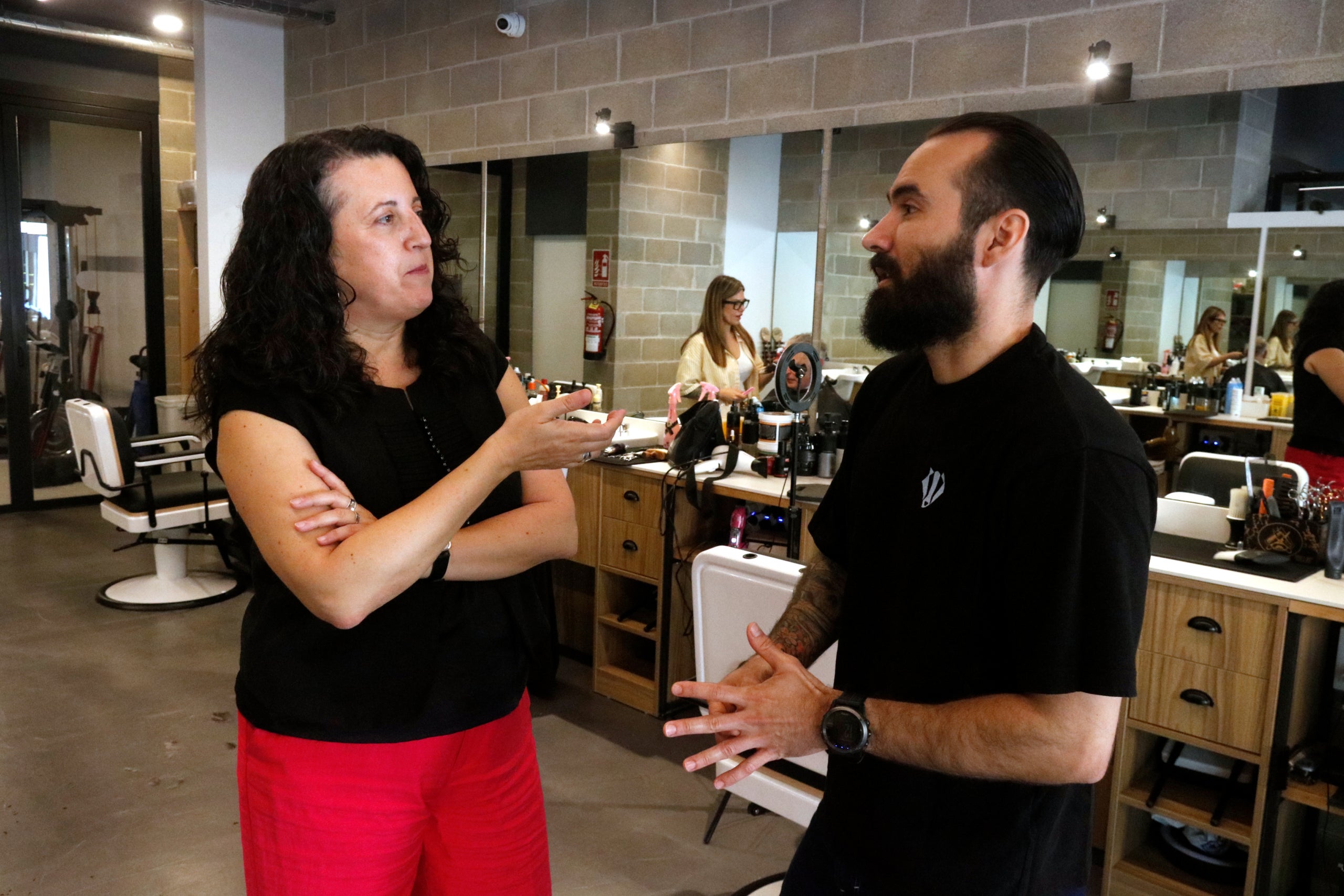 La concejala de Lengua Catalana de Girona, Núria Riquelme, y el barbero Pedro Barbella hablando en el interior de la peluquería Rut's Barberia & Tattoo de la Devesa de Girona / ACN