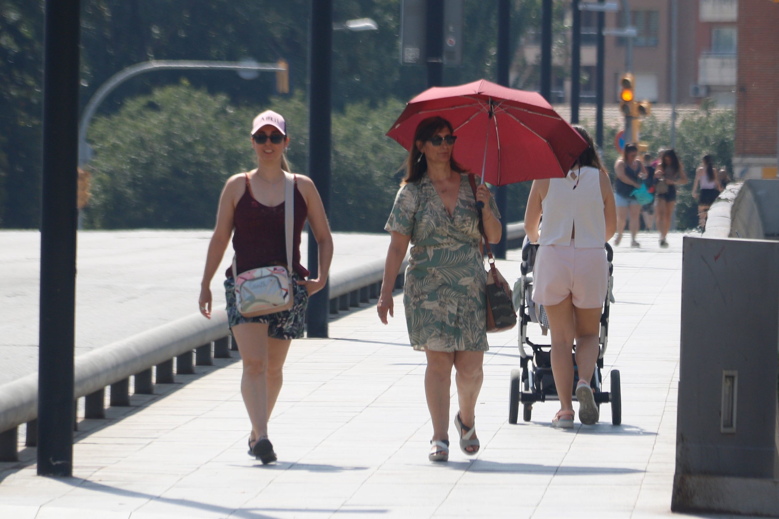 Una dona es protegeix del sol amb un paraigua i una altra amb una gorra, mentre caminen pel pont Vell de Lleida. | Roger Segura (ACN)