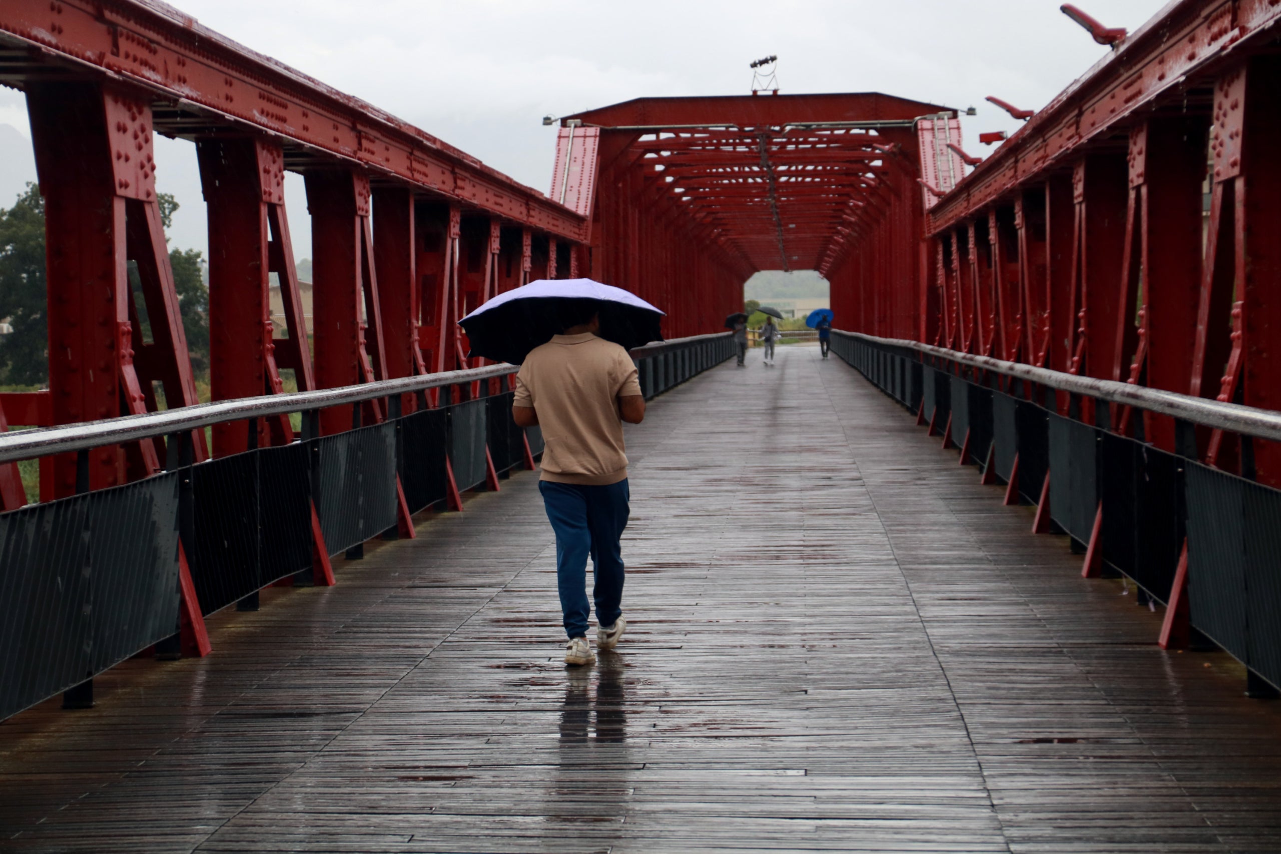 Un hombre caminando con un paraguas por uno de los puentes de Tortosa mientras llueve | ACN