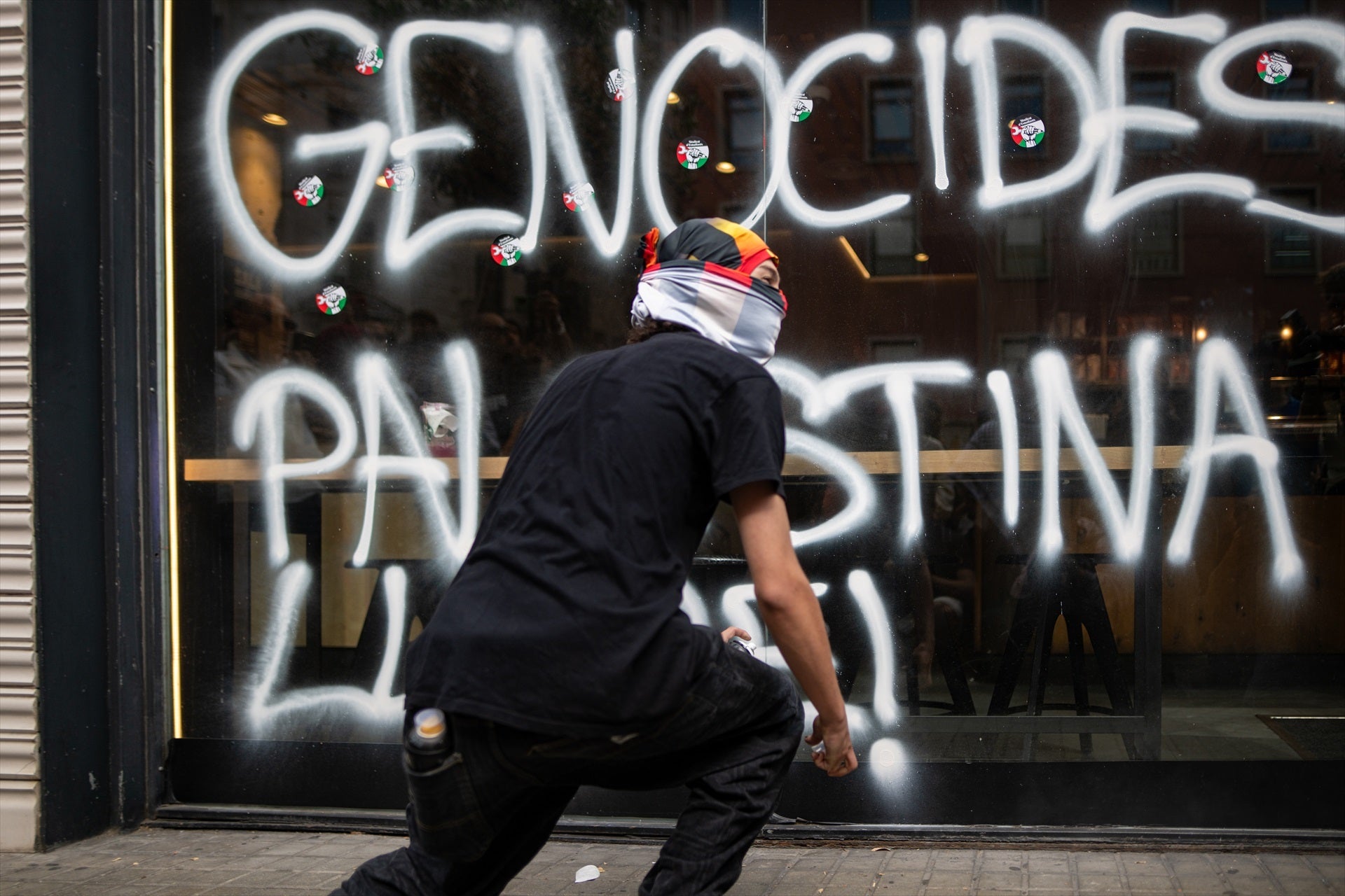 Un encapuchado hace una pintada contra Israel en un escaparate durante la protesta en Barcelona / Europa Press