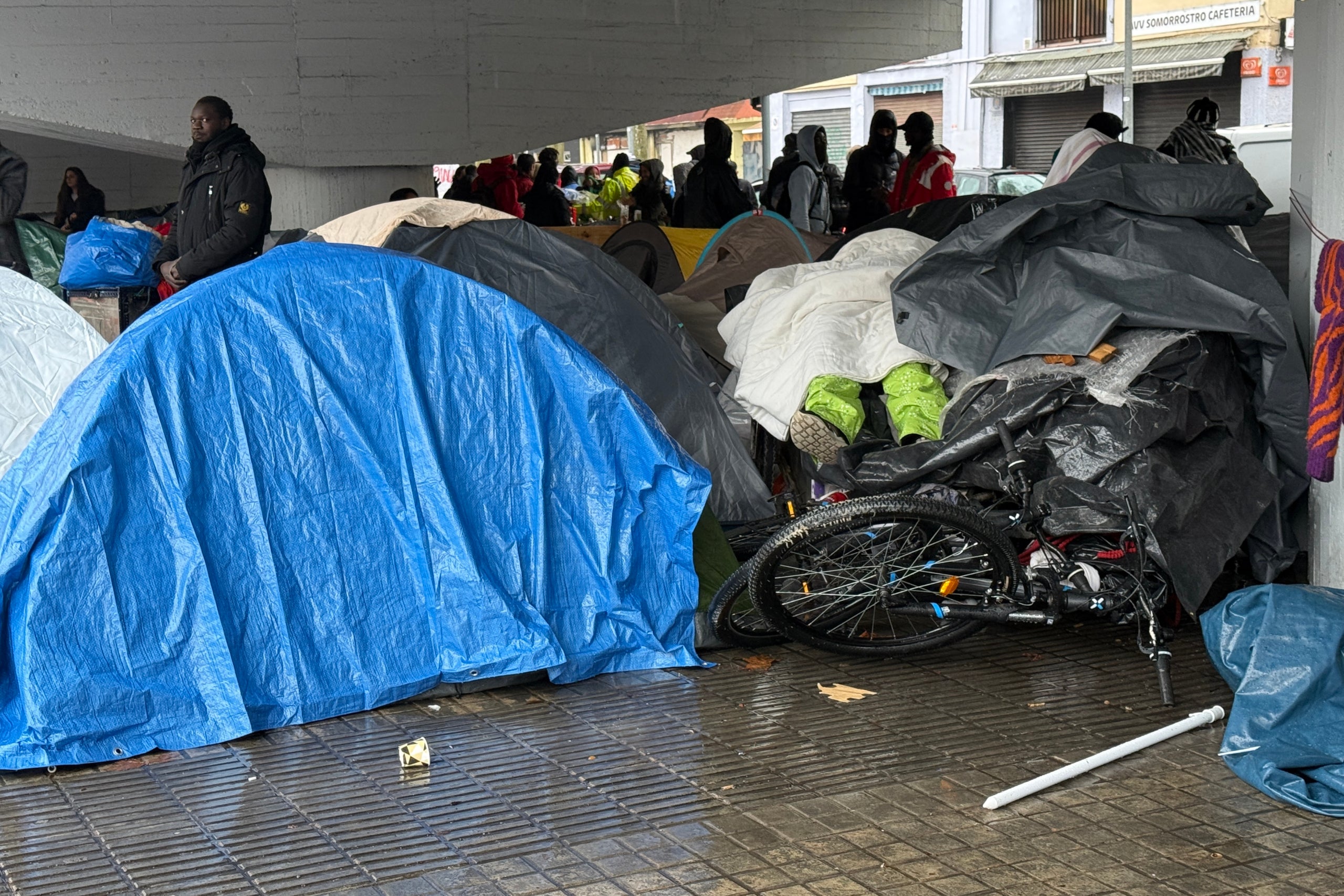 Una persona desallotjada del B9 dorm totalment tapada sobre material del campament sota la C-31. | Gemma Sánchez (ACN)