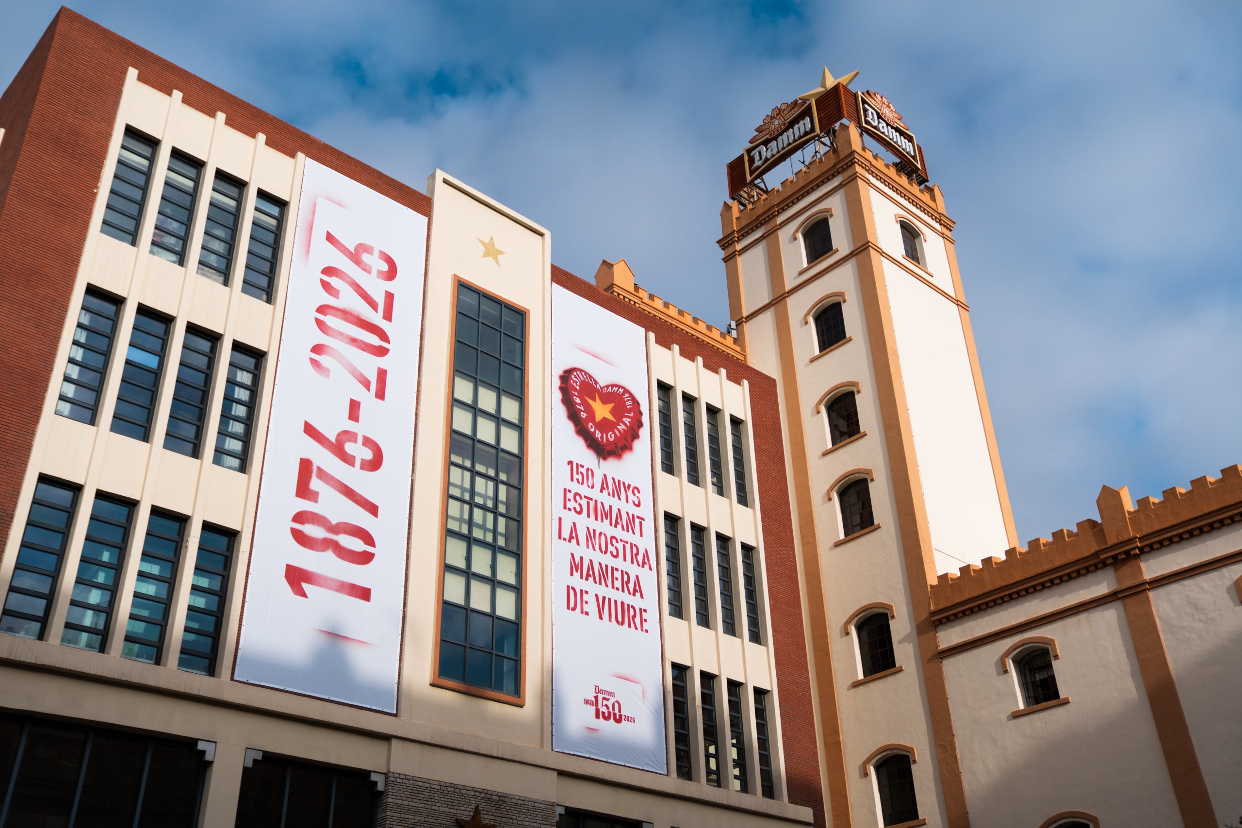 La façana de l’Antiga Fàbrica d’Estrella Damm ja llueix amb la campanya del 150è aniversari d’Estrella Damm, que inclou el logotip commemoratiu de l’efemèride | Estrella Damm