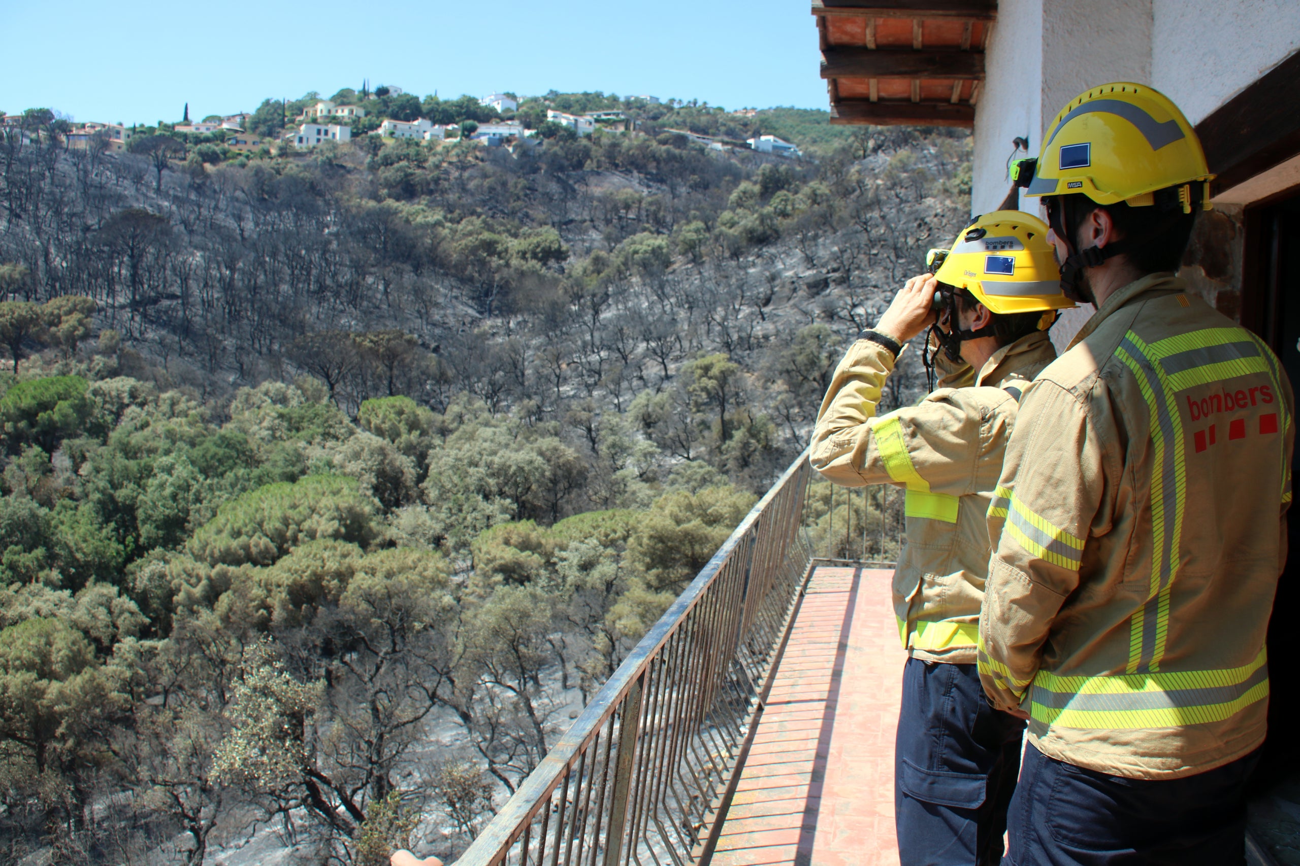 Els Bombers del GREC mirant amb prismàtics l'afectació de l'incendi de les Gavarres des d'una casa de la urbanització Mas Ambrós de Calonge | Xavier Pi (ACN)