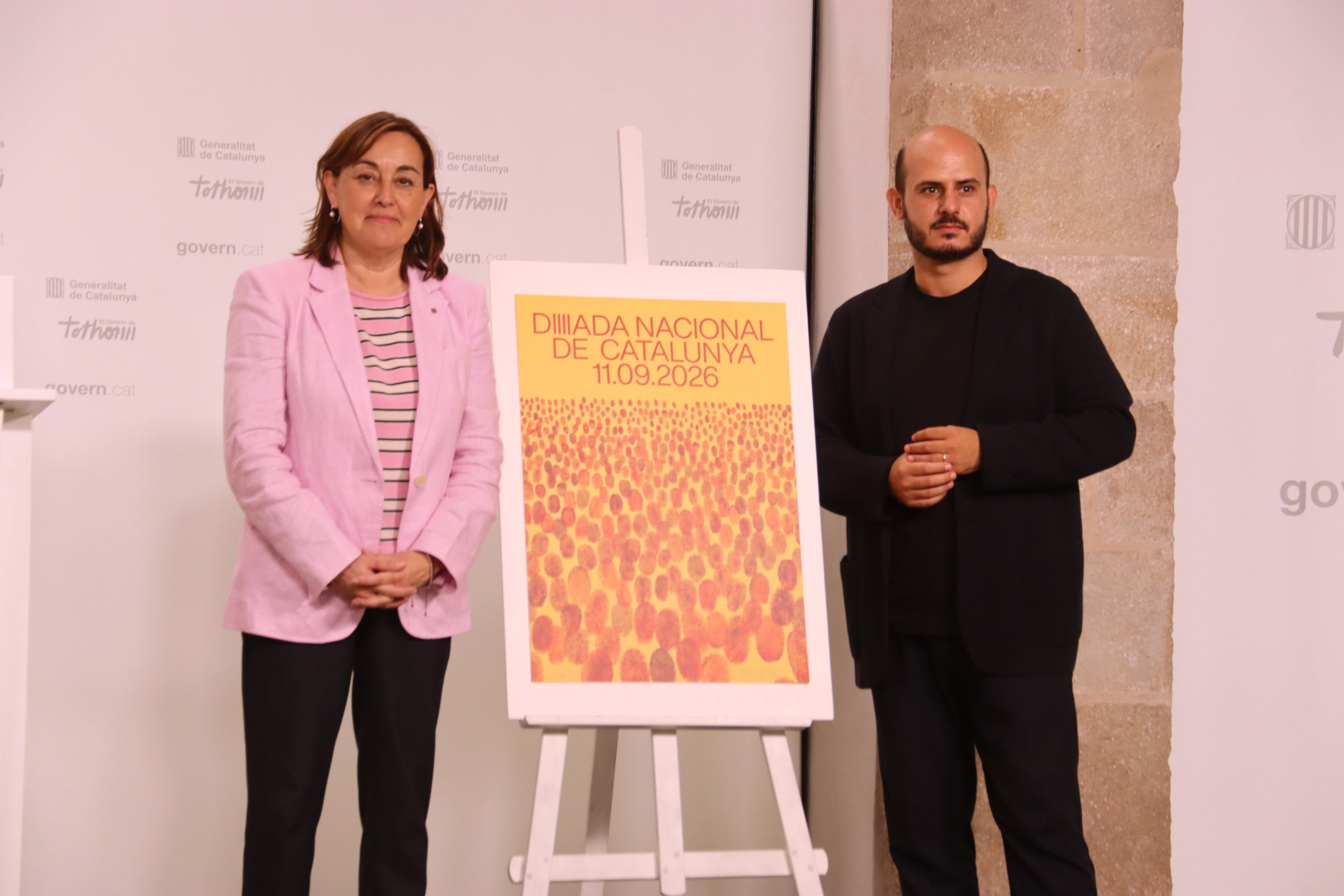 La portaveu del Govern, Sílvia Paneque, i el creador visual Javier Jaén al costat del cartell de la Diada del 2026 / ACN