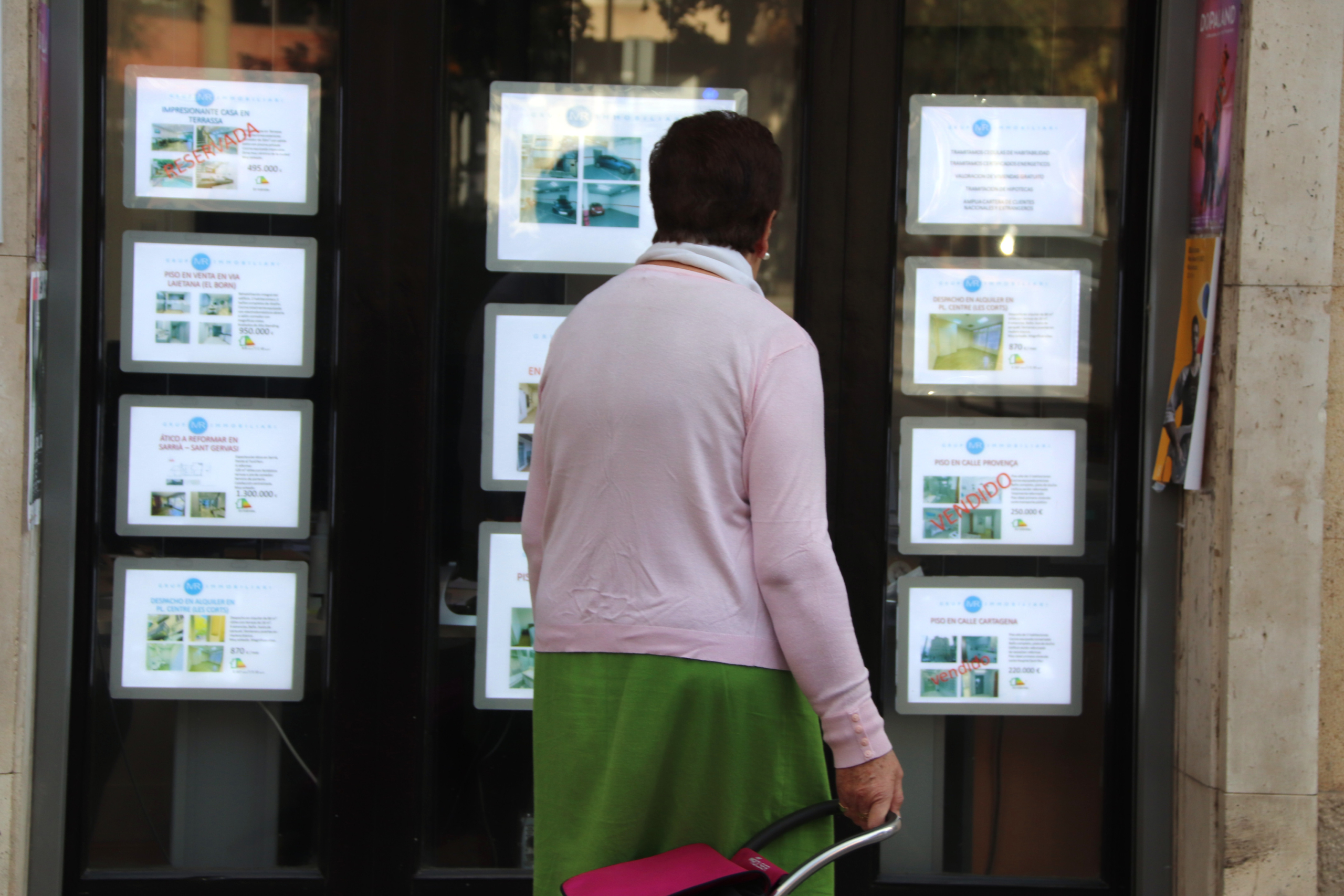 Una dona revisa les ofertes de pisos a la venda fora d'una immobiliària / ACN