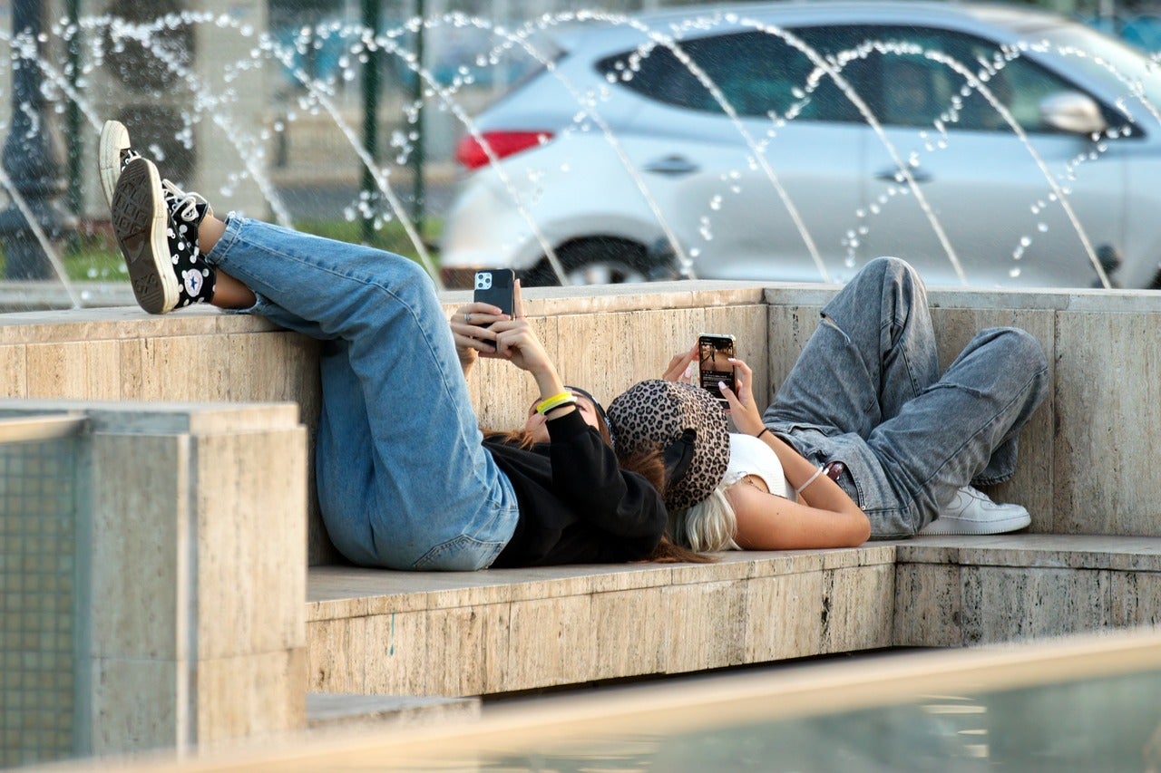 Dues noies joves estirades en un banc mirant el mòbil / Pixabay
