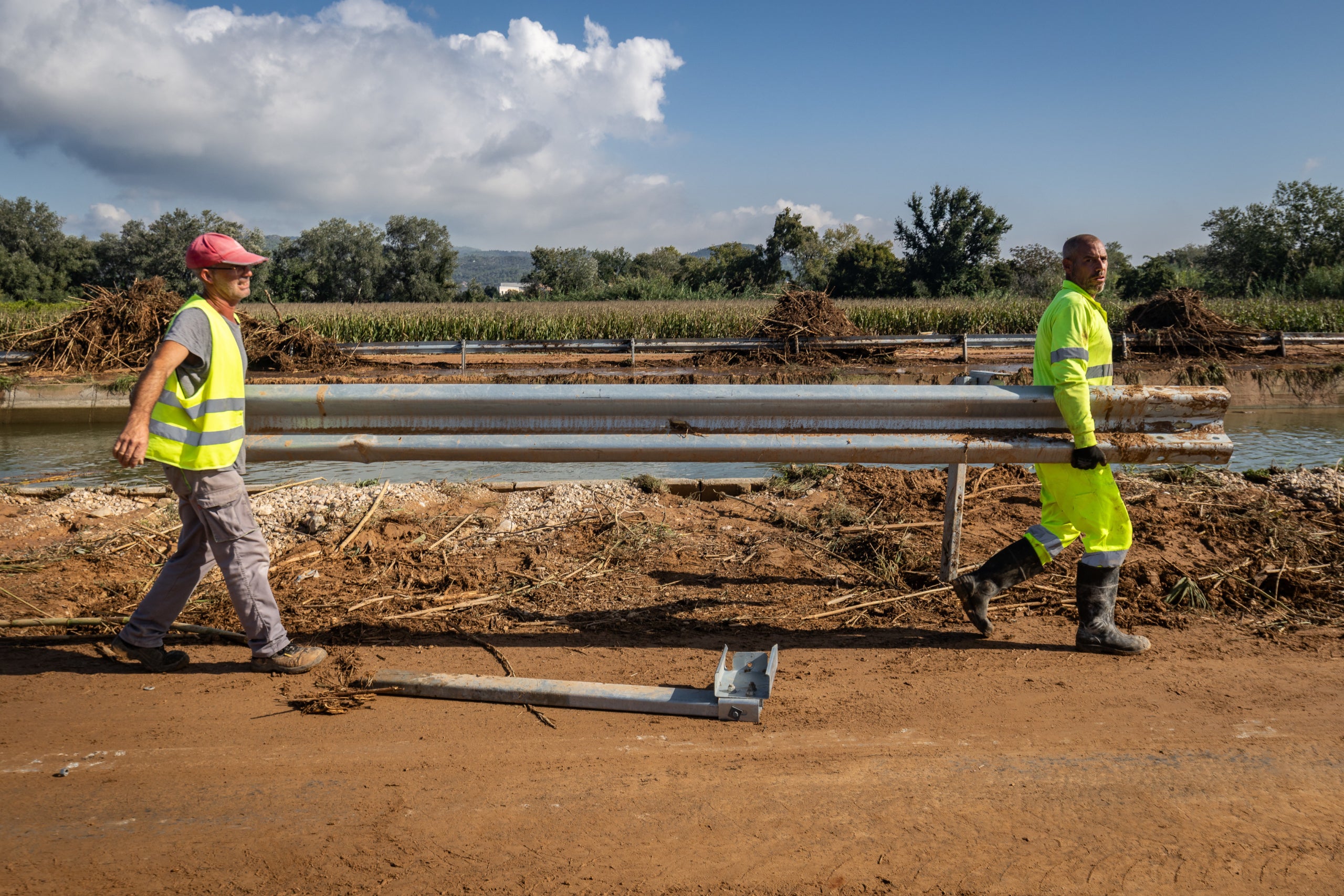 Dos operarios transportando una valla en una de las zonas afectadas por las inundaciones del Ebro en la carretera C-12, entre Amposta y Tortosa | Jordi Borràs (ACN)